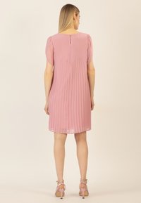 Rosa plissiertes Kleid mit kurzen, puffärmeligen Ärmeln, Knopfverschluss hinten und fließendem Stoff. Kombiniert mit hellrosa Riemchenheels.