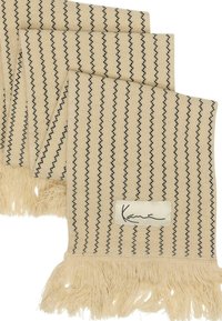 Beige vevd teppe med svarte vertikale striper, avsluttet med frynsede kanter og en hvit etikett med teksten "Kanu."