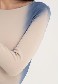 Maglietta a maniche lunghe con una superficie liscia. Presenta una sfumatura dal beige al blu, scollo rotondo e design aderente.