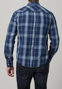 Námořnická károvaná košile na knoflíky, s světle modrými a bílými čtverci, dlouhými rukávy a zaobleným lemem. Vyrobena z bavlny, s bílými knoflíkovými detaily.