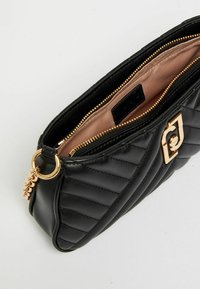 Clutch in pelle trapuntata nera con zip dorata, chiusura decorativa dorata e rivestimento interno in tessuto beige.