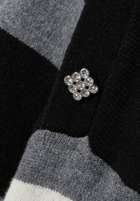 Spilla d'argento con nove cristalli trasparenti appuntata su un tessuto lavorato a maglia a righe nere e grigie.