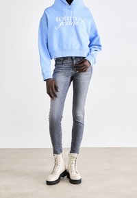 Sudadera azul recortada con el logo de "tommy jeans", combinada con jeans skinny grises y botas de combate beige con cordones y suelas negras.