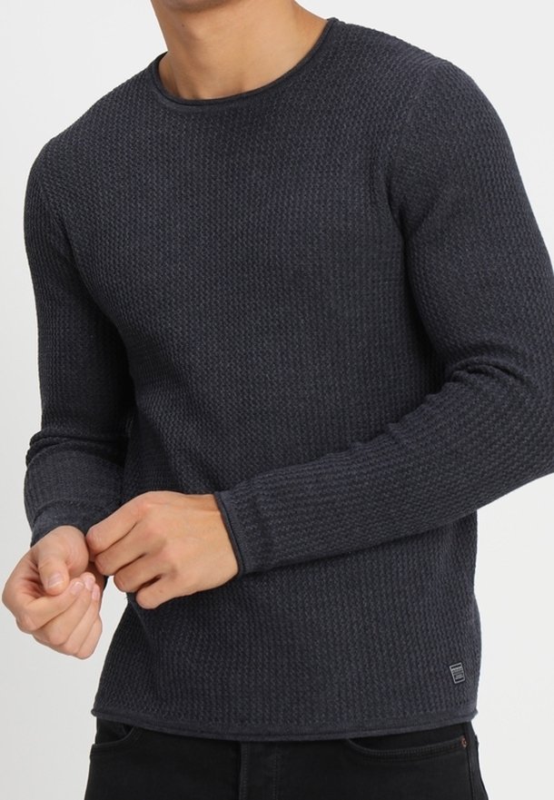 Ciemnoniebieski sweter z długim rękawem o teksturowanej powierzchni z okrągłym dekoltem i dopasowanymi rękawami. Posiada widoczne szwy oraz małe logo na hemie.