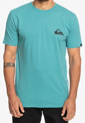 Turkusowa koszulka z krótkim rękawem wykonana z miękkiego materiału. Na piersi znajduje się czarne logo w kształcie góry, a dekolt ma standardowy okrągły krój.