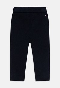 Pantalon en tricot bleu marine avec une taille et des poignets côtelés, arborant un petit logo brodé sur le côté supérieur. Texture douce, design à jambe droite.