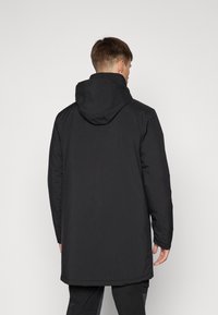 Jachetă neagră cu glugă, cu un finisaj mat și neted, având o croială lungă și un design minimalist. Fără buzunare vizibile sau embellismente.