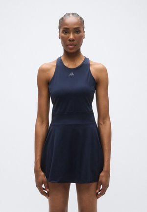 Vestido deportivo azul marino con parte superior ajustada y falda acampanada. Hecho de material liso y elástico. Presenta un logo sutil en la parte superior delantera.