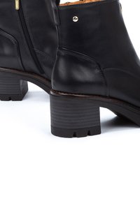 Botas de tobillo de cuero negro con tacón cuadrado estriado, cremallera lateral y detalles metálicos en dorado. Textura suave y líneas de diseño limpias.