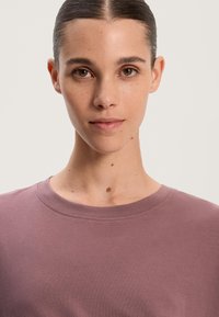 Lyse mauve kortærmet t-shirt med rund halsudskæring og glat tekstur, der har subtile stikninger på halsudskæringen.