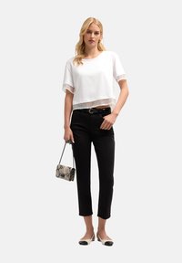 Camiseta blanca recortada con dobladillo de encaje transparente, combinada con pantalones negros ajustados. Accesorios con un pequeño bolso de estampado de serpiente y zapatos planos.