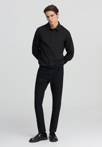 Czarna koszula z długim rękawem, zestawiona z czarnymi dopasowanymi spodniami i czarnymi skórzanymi butami. Gładka tekstura, zorganizowany design.