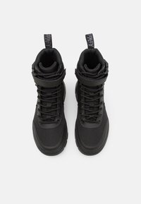 Zapatillas negras de corte medio, hechas de tejido texturizado y material sintético, con cordones en la parte delantera, cuello acolchado y correa para el tobillo.