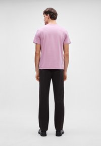 Lys rosa t-skjorte med korte ermer og rund hals, kombinert med svarte straight-leg bukser og svarte sko. Enkelt, avslappet design.