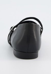 Bailarina de cuero negro con un tacón delgado, correa trasera y punta redondeada. Textura suave y diseño minimalista con una pequeña hebilla plateada.