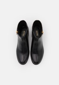 Bottines en cuir noir avec une finition lisse, bouts pointus et un accent de fermeture éclair dorée. La doublure intérieure est de couleur sombre. Design minimaliste.