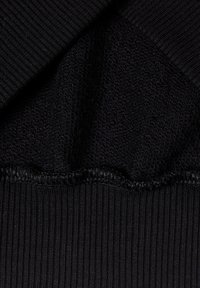 Detailní pohled na černou látku ukazující tři výrazné texturované vzory pletení a zkroucený šev, který je spojuje.