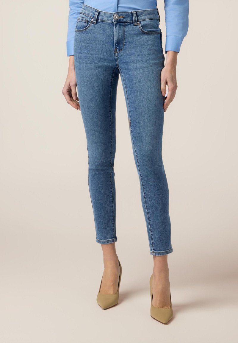 Jeans de denim azul ajustados con una cintura de media altura, que cuentan con un diseño de cinco bolsillos, un ligero desvanecimiento y un ligero deshilachado en el dobladillo.