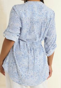 Jasnoniebieska bluzka wzorzysta z wzorami paisley, luźny krój, długie rękawy z podwinięciem oraz szczegół w postaci zawiązania w talii. Miękka bawełniana tkanina.