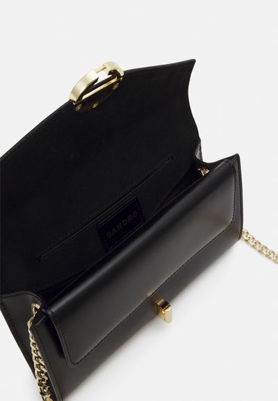 Borsa a tracolla in pelle nera con chiusura dorata e tracolla a catena. L'interno presenta una finitura liscia e un'etichetta nera con il marchio "SANDRO" impressa.