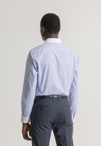 Camisa de vestir azul clara con mangas largas y puños blancos, combinada con pantalones azul marino que presentan un cinturón y detalles en el bolsillo trasero.