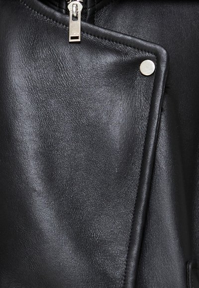 Zwart leren jack met een gestructureerde afwerking, asymmetrisch ontwerp aan de voorkant, zilveren rits en metallic drukknopdetails.