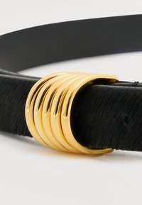 Cinturón negro texturizado con una hebilla curva dorada lisa que presenta cinco estrías paralelas, mostrado sobre un fondo blanco.