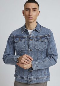 Denimska jakna svijetloplave boje, klasičnog kroja, s dva džepa na prsima i kopčanjem na gumbe. Tekstura tkanine s blagim izbljeđivanjem.