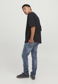 T-shirt oversize nera, jeans blu e sneakers nere. La t-shirt ha maniche corte e una vestibilità rilassata; i jeans presentano lievi sbiadimenti e tasche posteriori.