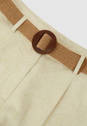 Beżowe teksturowane spodnie z plisami, wyposażone w szeroki pleciony brązowy pasek z dużą okrągłą brązową klamrą w talii.