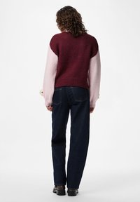 Πλεκτό πουλόβερ με μπλοκ χρωμάτων σε μπορντό και ανοιχτό ροζ, ριμπ τελείωμα και μακριά μανίκια. Συνδυάζεται με σκουρό μπλε τζιν με ίσια γραμμή και μαύρα παπούτσια.