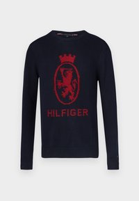Maglione lavorato a maglia blu navy con un grande emblema rosso di leone e la scritta "HILFIGER". Girocollo, maniche lunghe e polsini e orlo a coste.