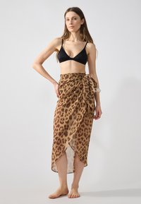 Jupe portefeuille à imprimé léopard en tissu léger et transparent ; elle dispose d'un lien à la taille et d'une fente haute pour un mouvement facile. Haut de bikini noir.
