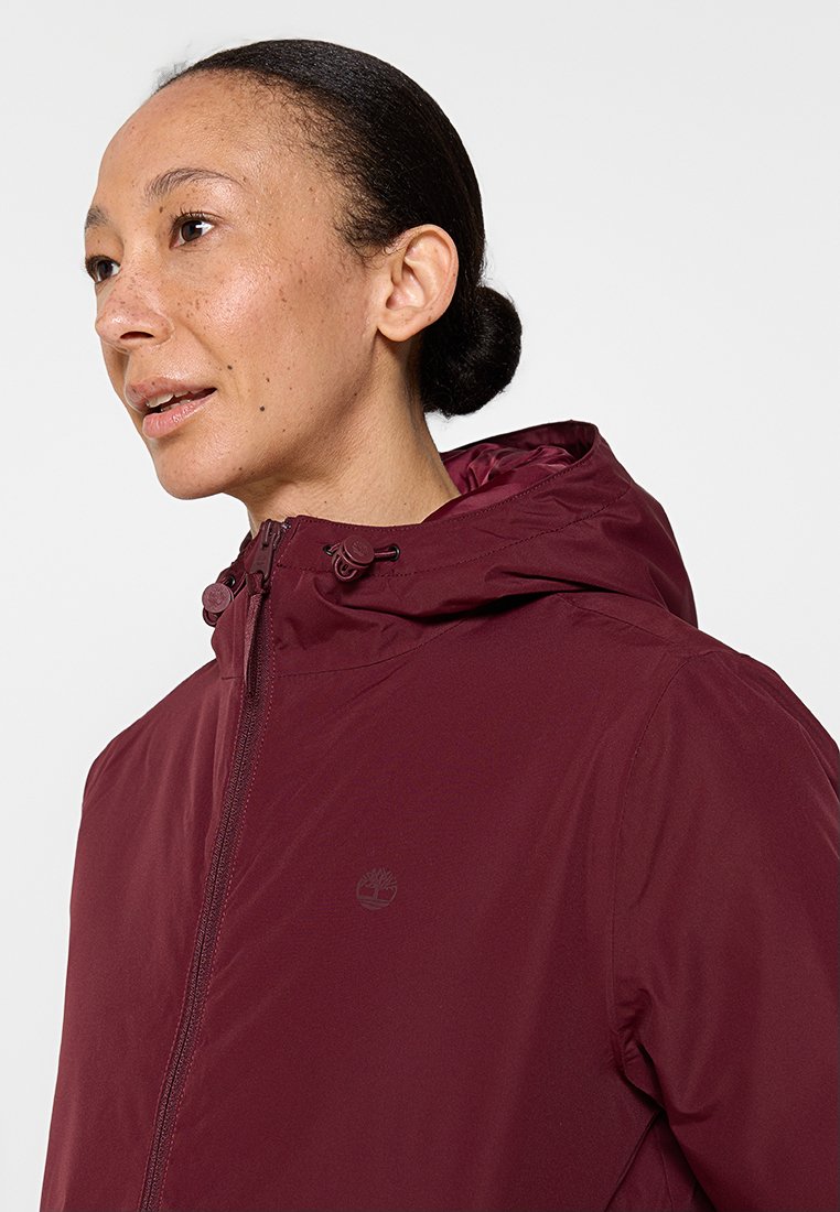 Chaqueta con capucha burdeos con cierre de cremallera, hecha de material ligero. Cuenta con cordones ajustables en la capucha y un acento de logo.