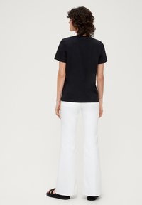 Schwarzes T-Shirt mit kurzen Ärmeln und rundem Halsausschnitt, kombiniert mit weißen Schlagjeans und schwarzen Sandalen. Glatter Stoff, lässige Passform.