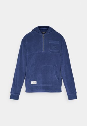Marineblå fleecehette med frontglidelås, stor kengurulomme, liten brystlomme og broderte detaljer på lommen. Myk tekstur.