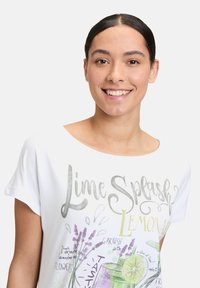 Biała koszulka z krótkim rękawem z napisem "Lime Splash Lemonade" w kolorze szarym, z ilustracjami lawendy i wzorem szklanki na napój.