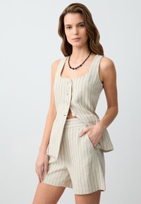 Lichtbeige tweedelige outfit van textuurstof met verticale strepen. De top heeft een ronde hals, knopen en een peplumstijl, gecombineerd met shorts.