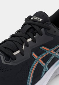 Zwarte sportschoen met een gestructureerde bovenkant, oranje en teal accenten, en een gevoerde zool met veters en een logo op de tong.