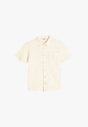 Chemise blanche à manches courtes avec un motif texturé, devant boutonné, col etune poche poitrine unique. Les boutons sont de couleur beige clair.