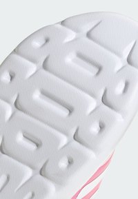 Podeszwa buta z teksturowanej białej gumy, z wypukłymi, sześciokątnymi wzorami; różowe akcenty wzdłuż krawędzi.