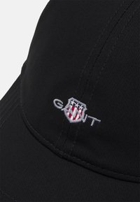 Zwarte baseballcap van katoen twill, met een gestikt GANT-logo met rode en witte accenten op een schild, en een gebogen klep.