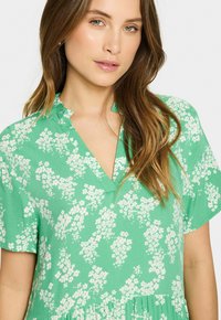 Rochie verde cu mânecă scurtă, cu decolteu în V, având un model floral în alb și roz deschis. Material moale, cu o croială lejeră.