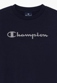 Tummansininen collegepaita, jossa on ribattu pyöreä pääntie. Paidassa on iso valkoinen "Champion"-logo tekstuurilla rintamuksessa.