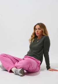 Maglione grigio, pantaloni in pile rosa e sneakers grigie. Il maglione ha una consistenza morbida e maniche lunghe; i pantaloni sono comodi e larghi.