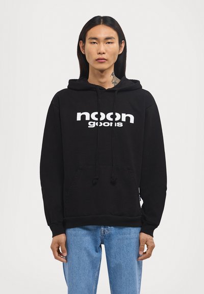 Schwarzer Baumwollhoodie mit einer Kängurutasche vorne, einer verstellbaren Kapuze und dem "noon goons"-Logo in weißem Druck auf der Brust.