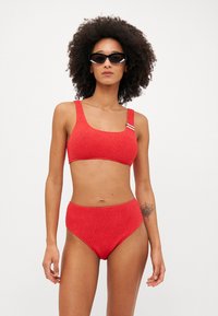 Rød teksturert bikini med et rektangulært crop top med brede stropper og høyt liv på bunnen. Minimalistisk design med en sporty følelse.