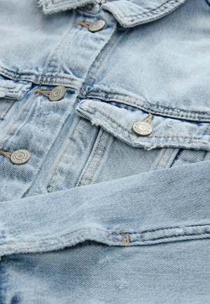 Helle blaue Jeansjacke mit Metallicknöpfen, frontalen Taschen und fransigen Kanten. Die Textur des Stoffes ist weich und hat einen leicht abgetragenen Look.