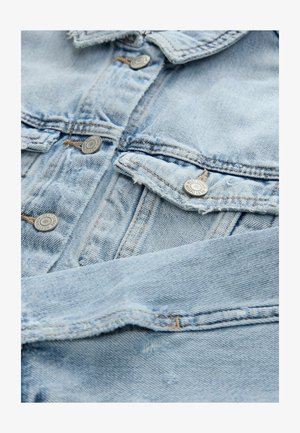 Chaqueta de mezclilla azul claro con botones metálicos, bolsillos frontales y bordes deshilachados. La textura de la tela es suave y tiene un aspecto ligeramente usado.