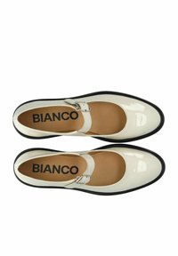 Zapatos Mary Jane de charol blanco con suela negra, con punta redonda y correa con hebilla plateada. Nombre de la marca "BIANCO" visible en el interior.